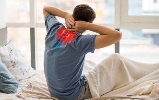 A young man sitting in bed with neck pain.