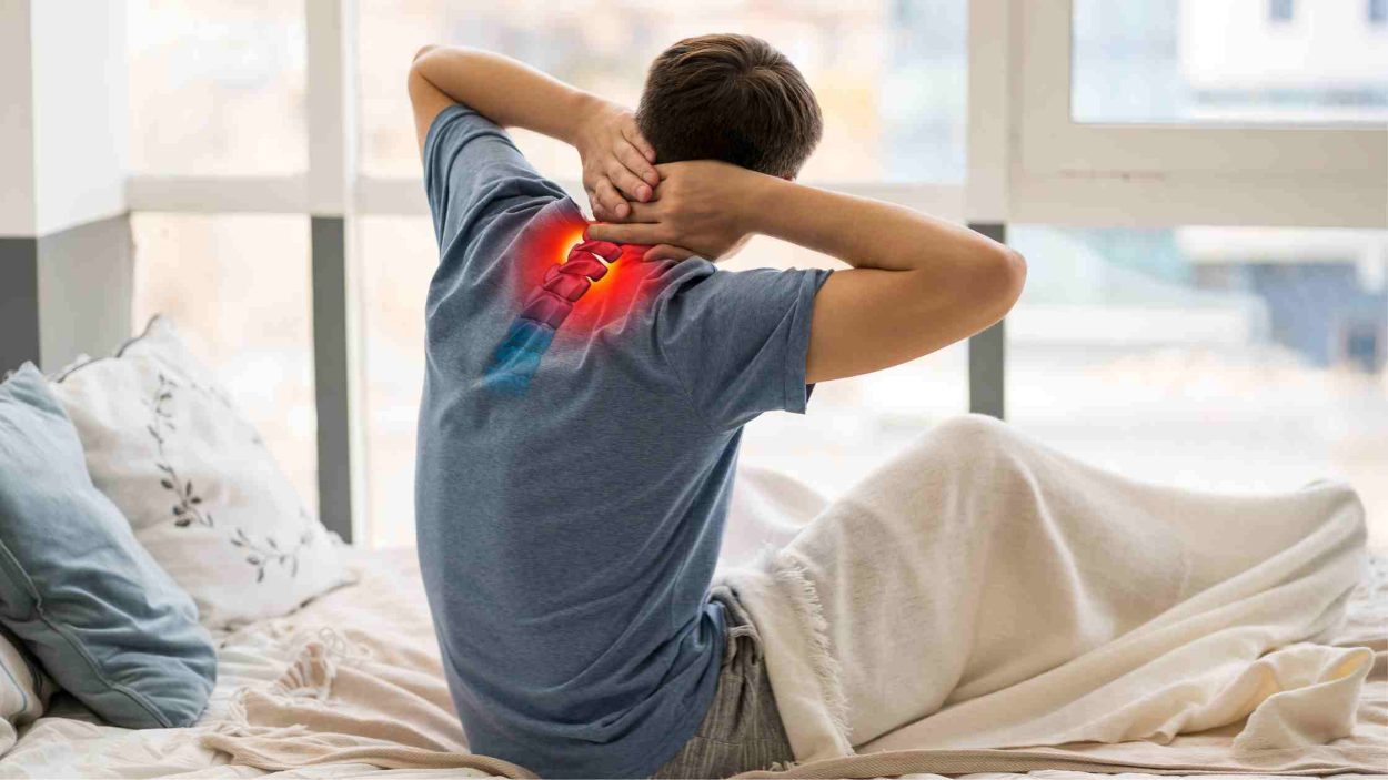 A young man sitting in bed with neck pain.