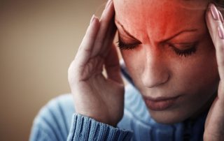 A close-up of a woman holding her head in her hands because of a headache.